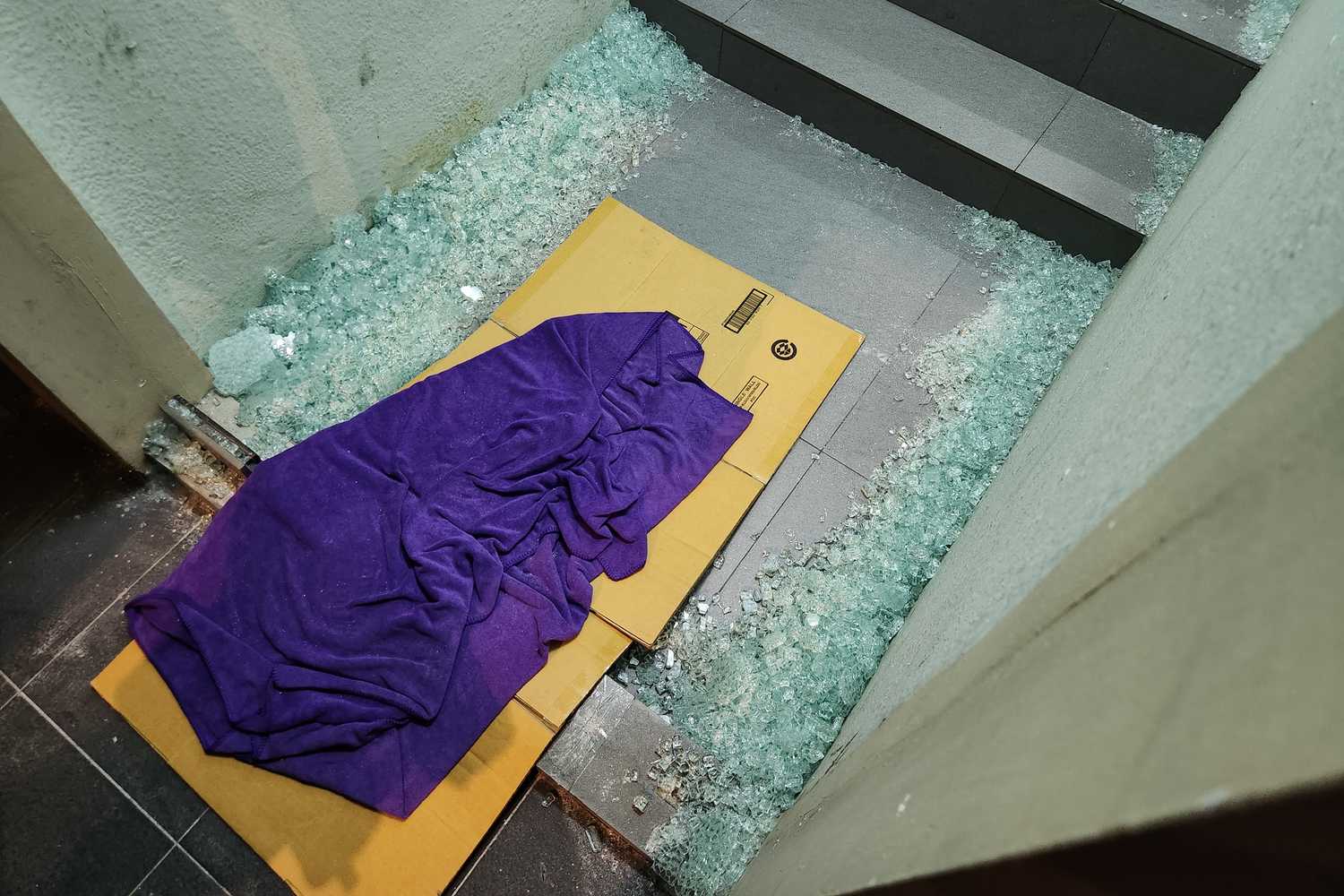 an image of a broken glass door shattered on the floor, with a cardboard placed on it for officers to walk across