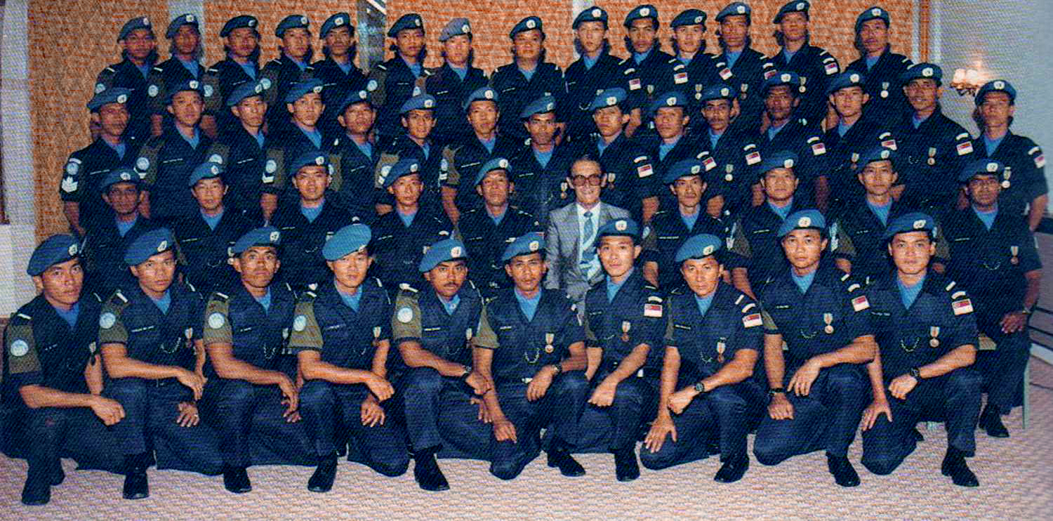 police officers in a group photo, all wearing police uniform and sporting blue coloured berets. In the middle there is a caucasian man in a grey suit, who is the CIVPOL commissioner. 