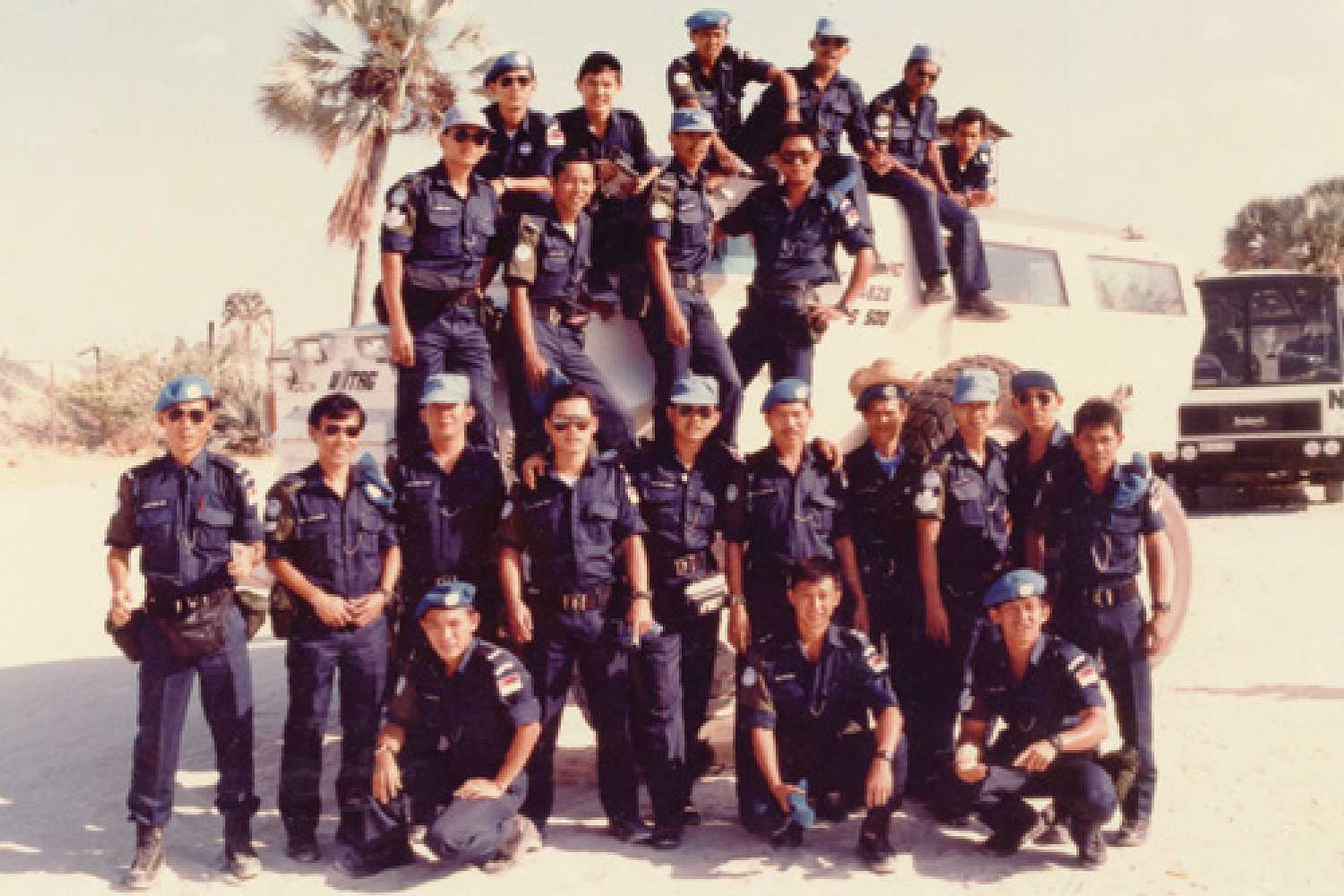 group of police officers in the desert, posing with a white colour Armoured Personnel Carrier, with some officers seated on top. 