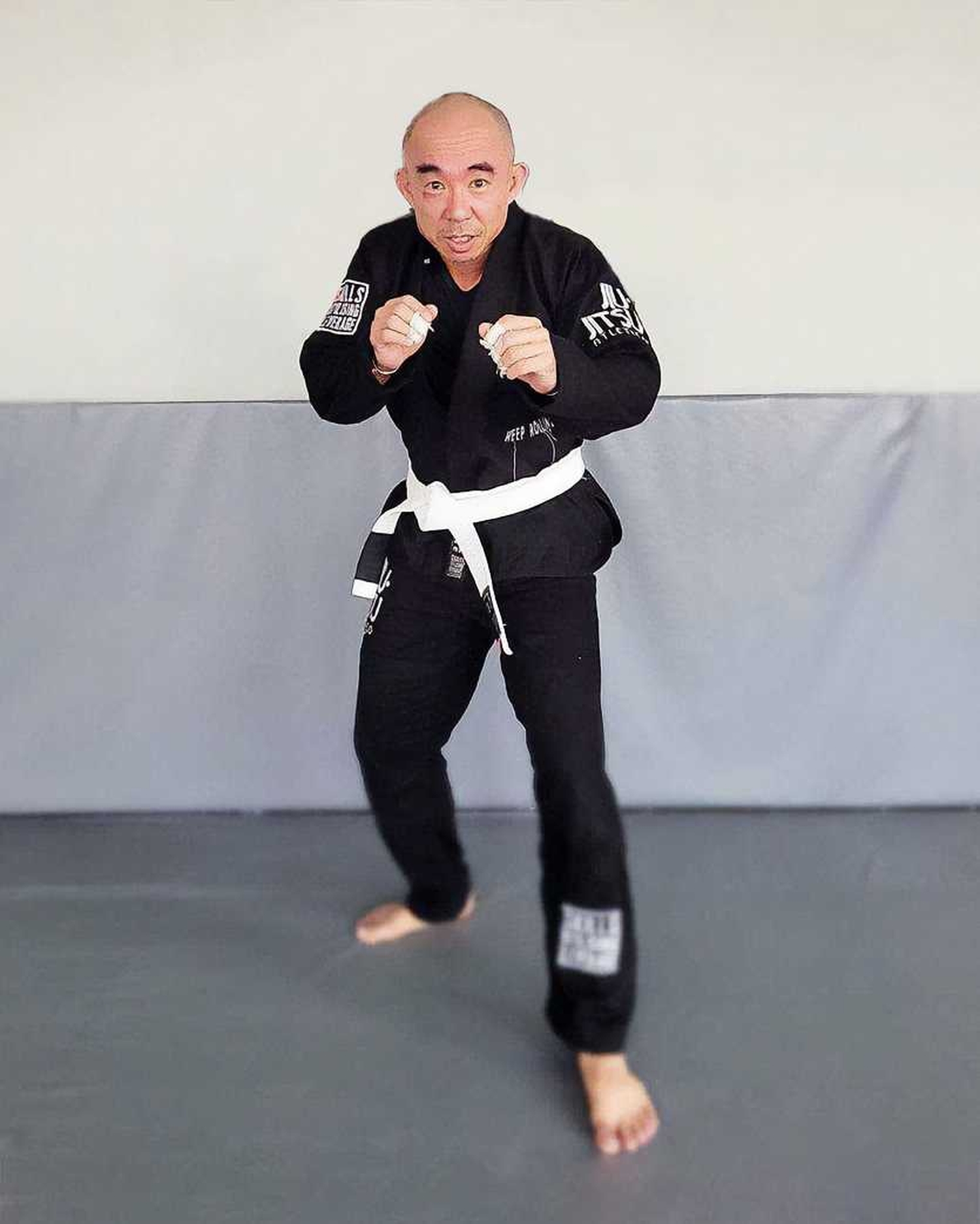 Inspector Tan Buck Song facing the camera, donned in his black martial arts uniform and white belt around his waist, posing in a martial arts stance, his left foot in front of his right, and his fists propped up.