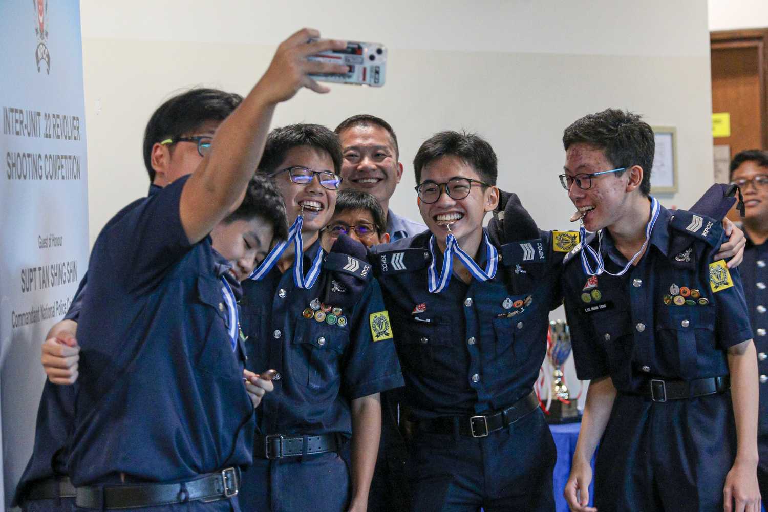 Group of male NPCC Cadets posing by biting their medals, and taking a selfie with their Teacher Officer excitedly after the award ceremony ended.