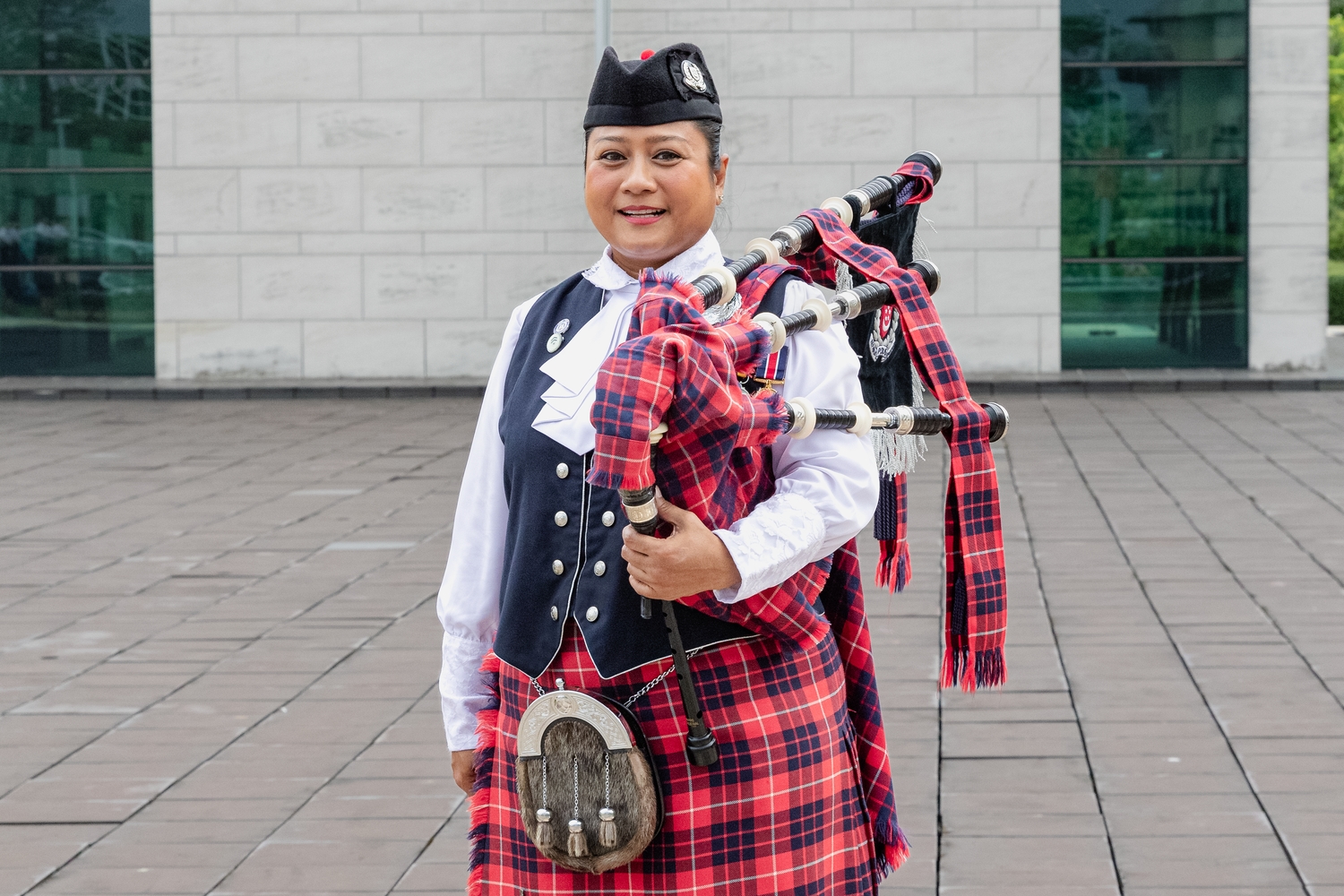 SI Julizah Binti Kassim stands smiling in front of the camera, holding her bagpipe over her shoulder in her WPPD performance uniform