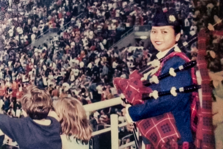 An old vintage photo of SI Julizah Binti Kassim at the 1998 Rugby Seven Asian Games held in Hong Kong. She is holding her bagpipe and wearing her WPPD uniform while looking over the shoulder in front of a large crowd by a railing. 
