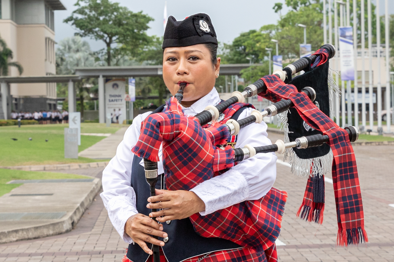 SI Julizah Binti Kassim looking into the camera in her WPPD uniform and blowing into the bagpipe to inflate air into it. This is what she does before playing the bagpipe by harnessing the reeds and drones. 