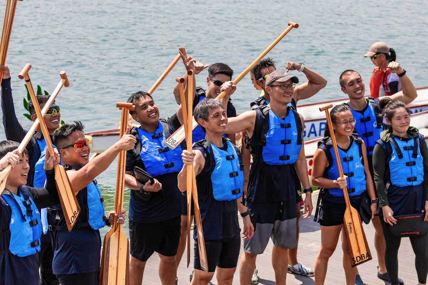 a group of dragonboaters in their life vests and holding paddles smiling and cheering