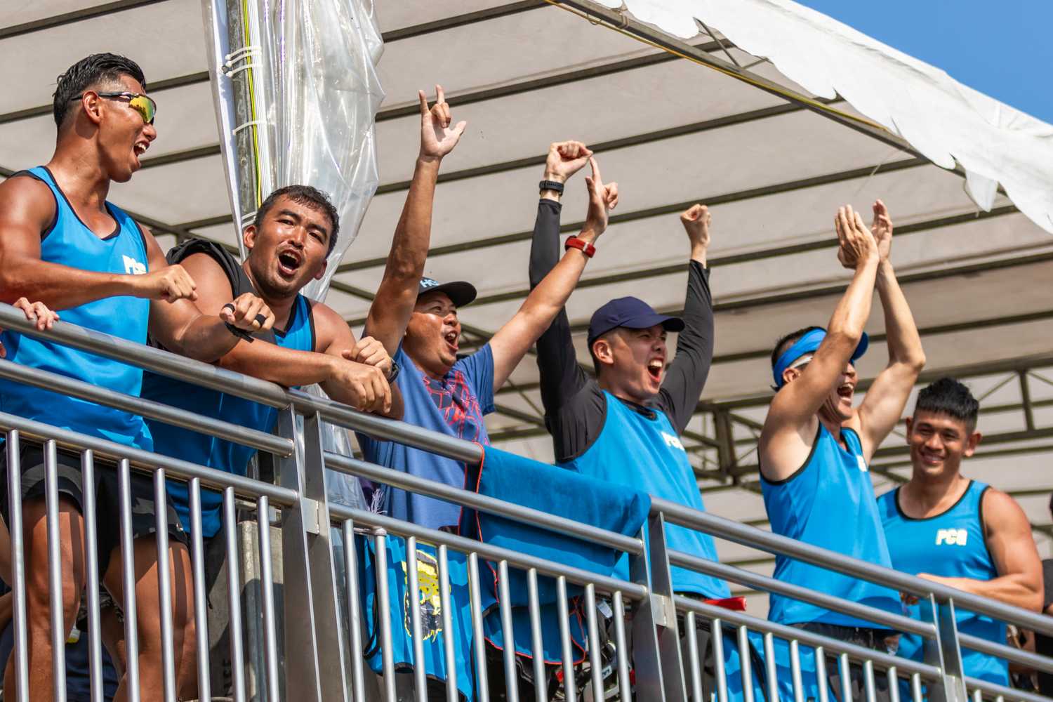 spectators along the shoreline with arms raised and cheering as they lean on the railings