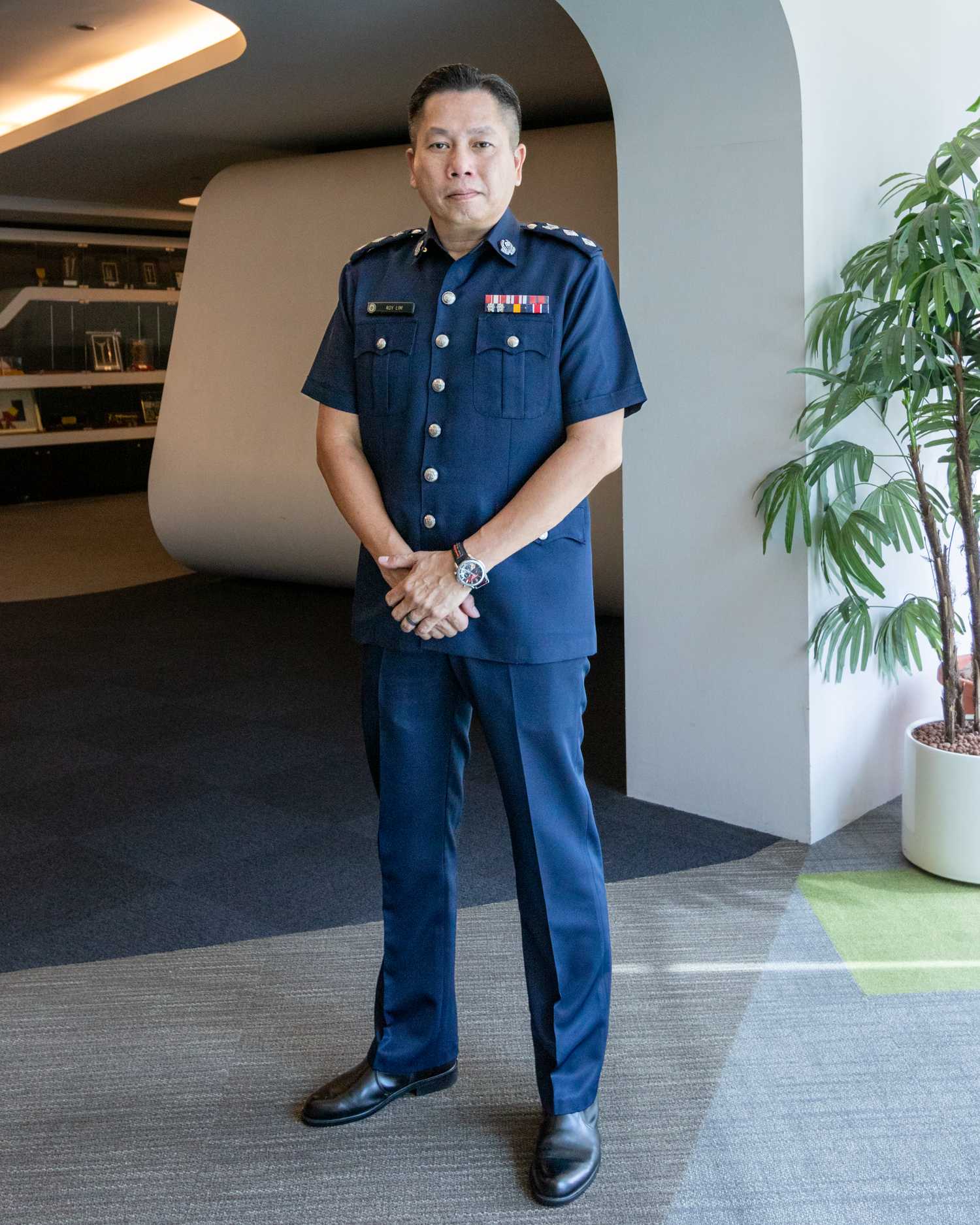 Superintendent of Police (Supt) Roy Lim is standing proudly looking at the camera in a profile shot, with his hands neatly placed in front of him.