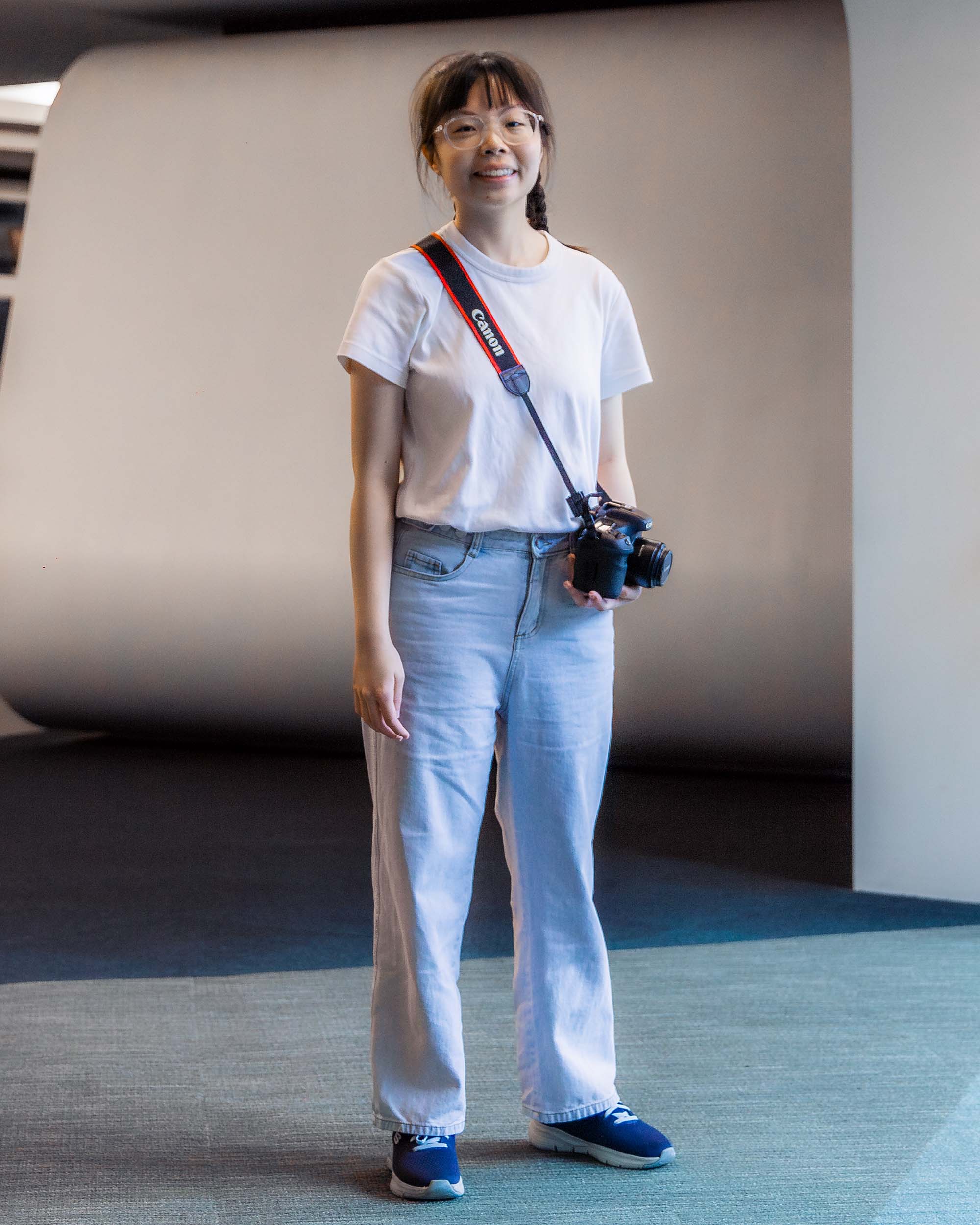 A portrait shot of Amanda Wong. She is standing and has a camera strapped to her neck with a lanyard. Her left hand is supporting the camera.