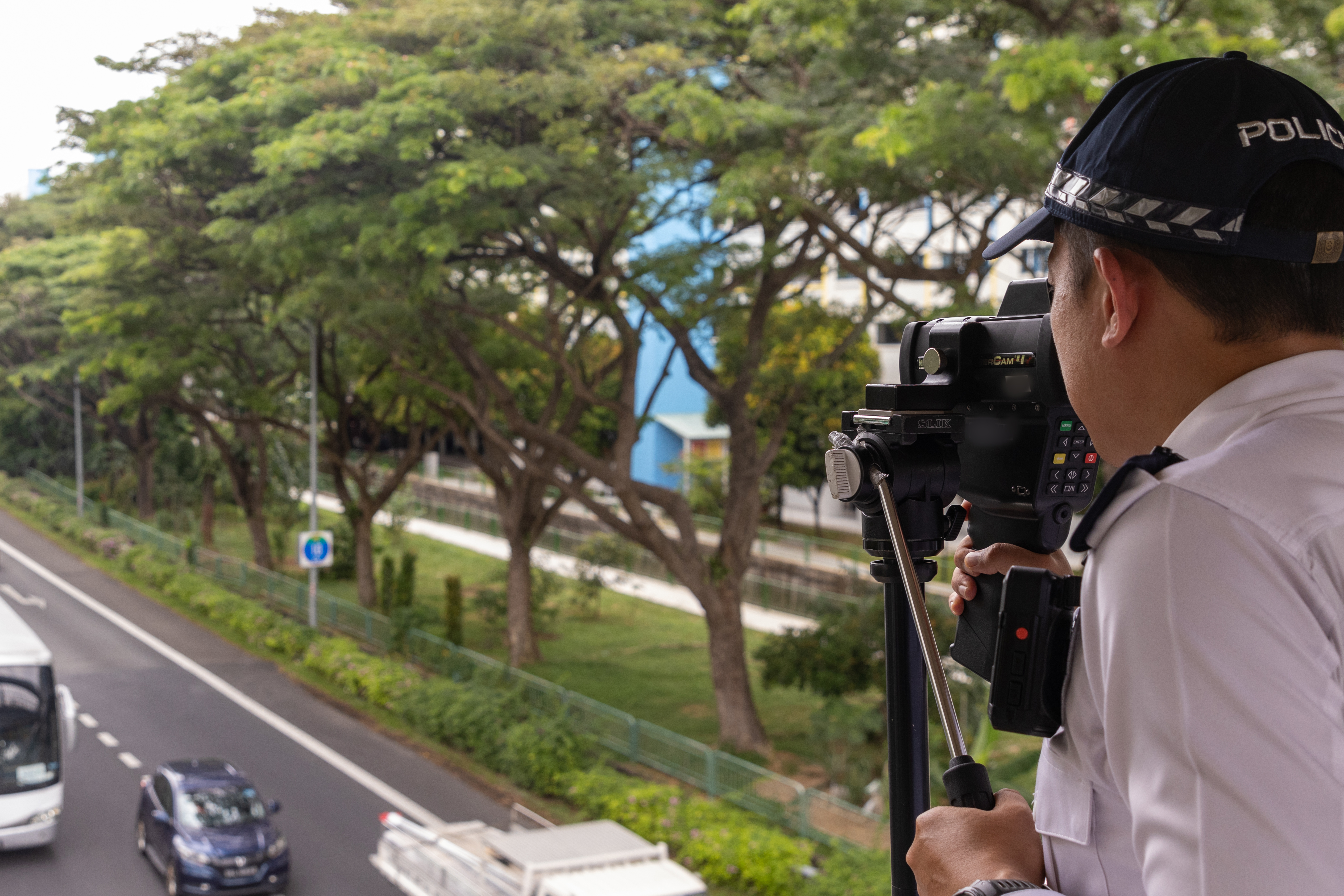 A Traffic Police officer using an enforcement camera to capture speeding vehicles from overhead bridge