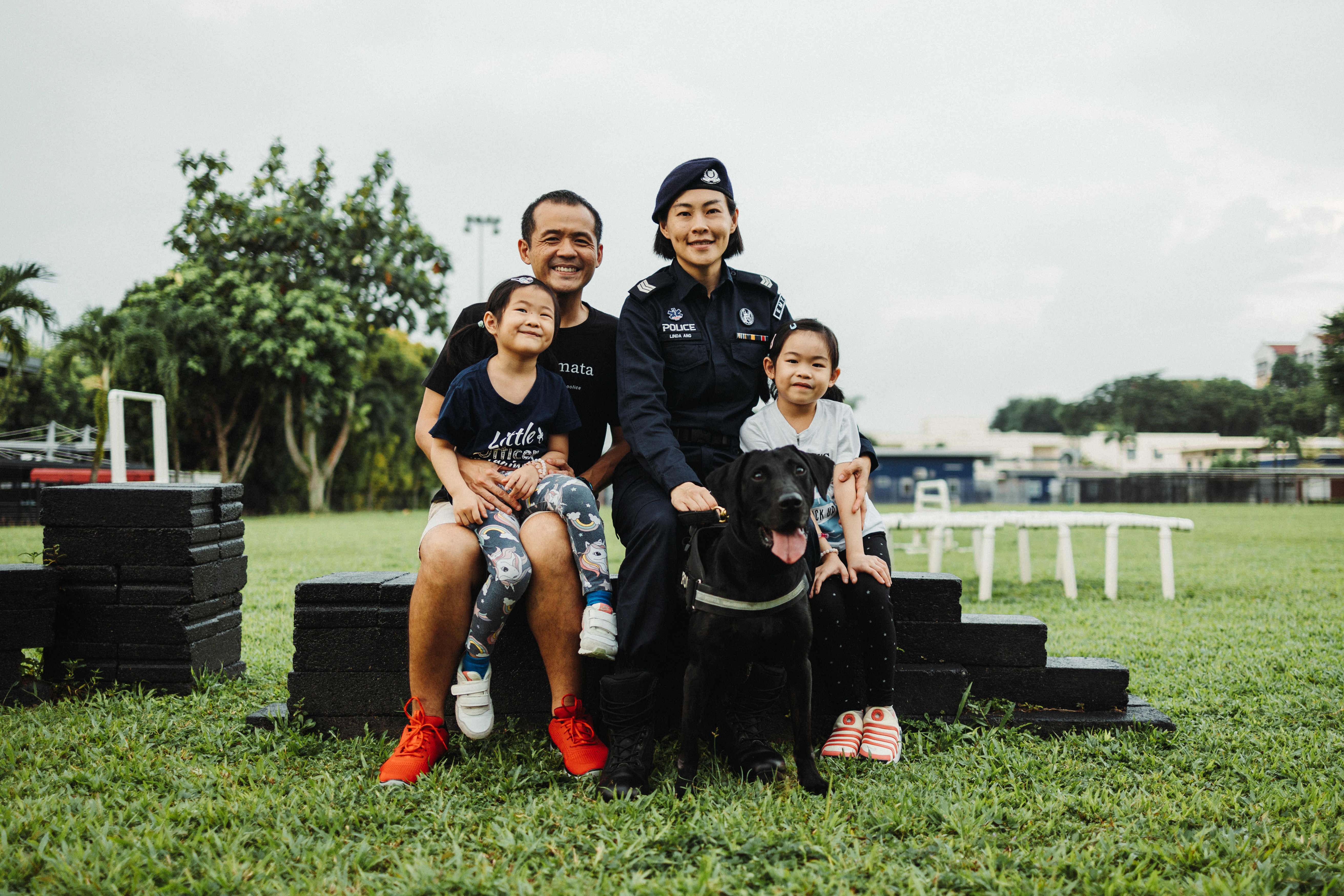 family sitting together on a field of grass, on top of a dog obstacle element