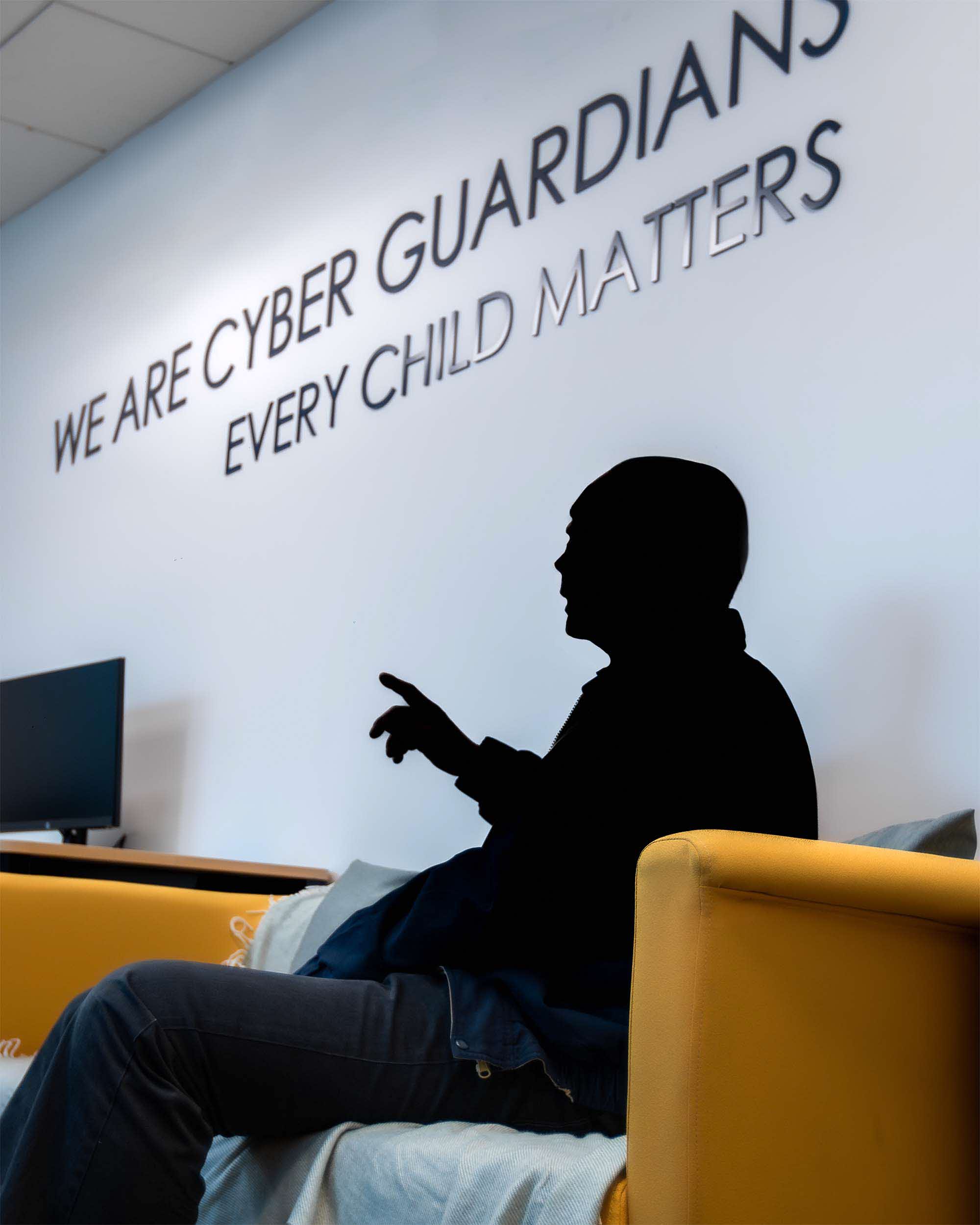 a fully black figure, censored, sitting on a yellow couch in an office setting