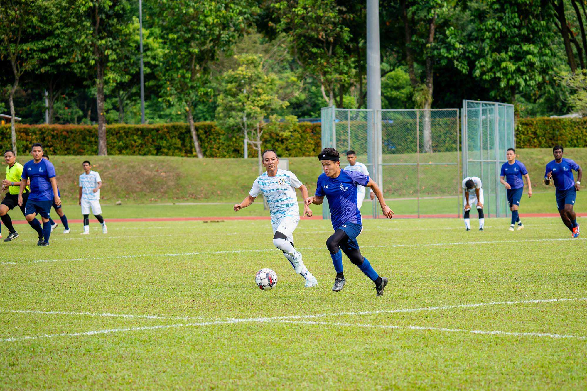 footballers running on a football pitch, with some wearing light blue and the others wearing dark blue