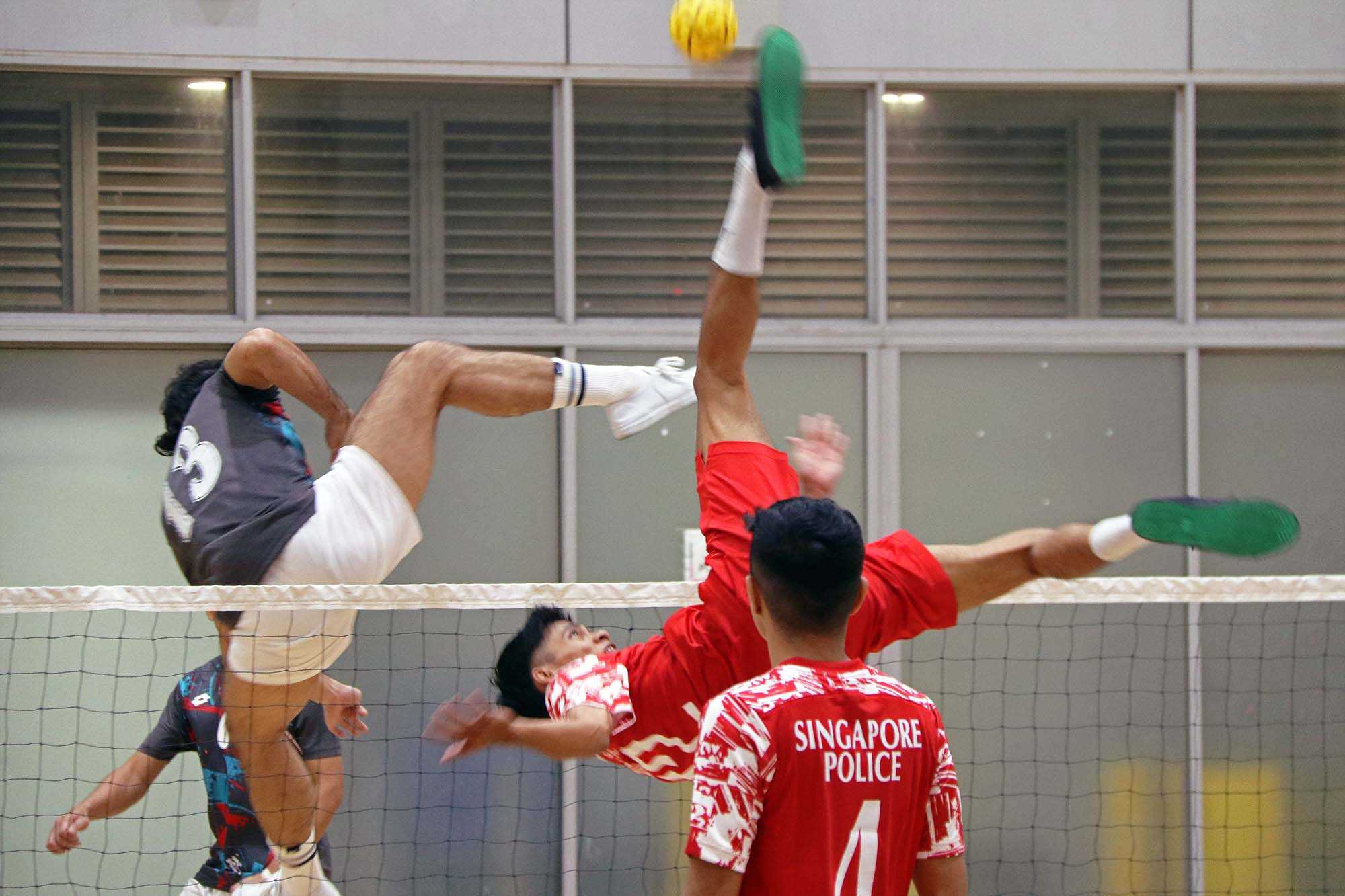 sepak takraw players competing against each other with one player doing a somersault to shoot the ball