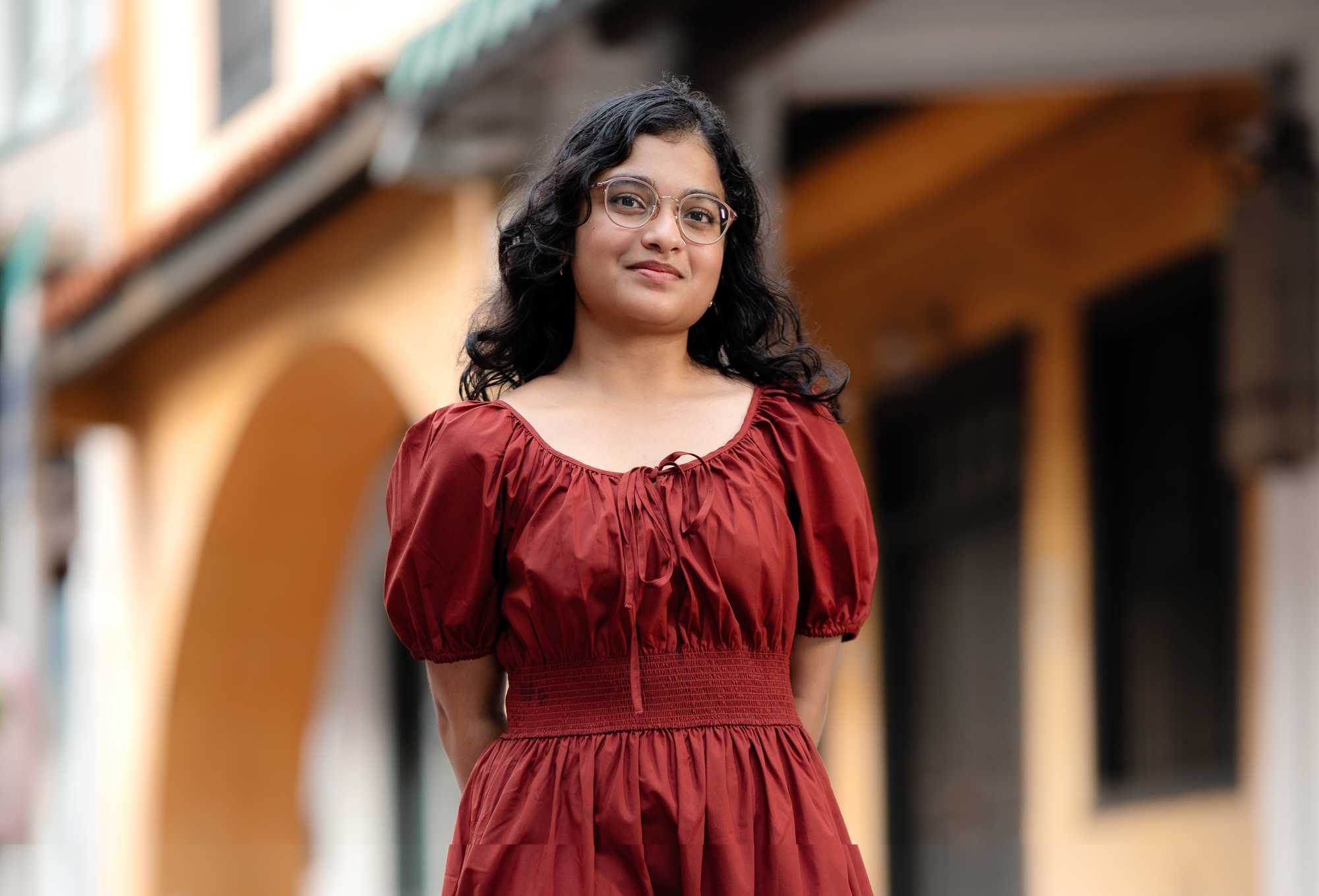 photo of a young girl wearing red looking at camera, with her arms behind her back