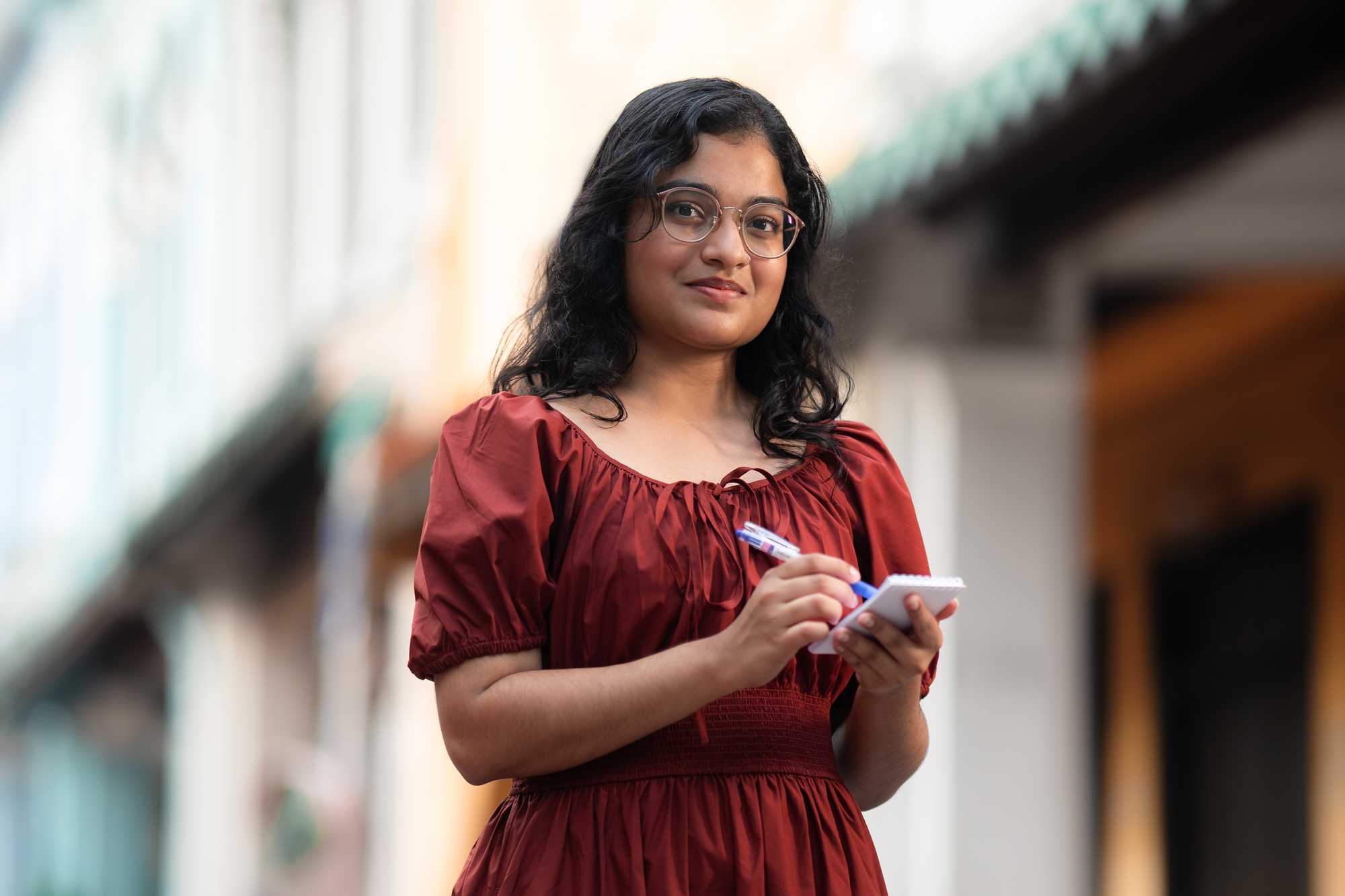 photo of woman in red dress holding pen and writing on notepad, while smiling at camera