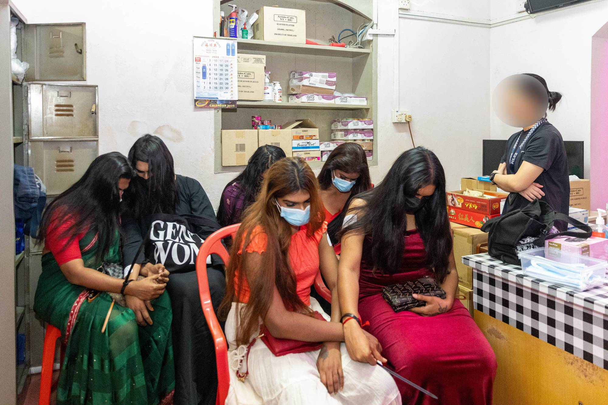 a photo of 6 individuals sitting in traditional indian clothing, with their long hair covering their face, as an officer on the right is looking at them